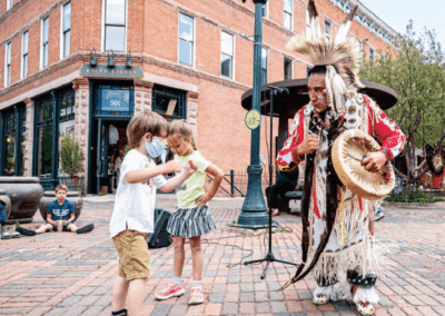 Children interacting with an Native American performer on a city street.